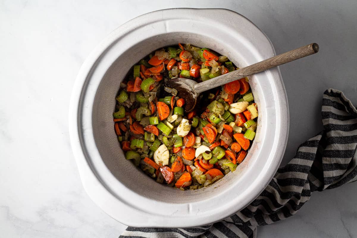 Large crock pot insert filled with carrots celery onion herbs and garlic 