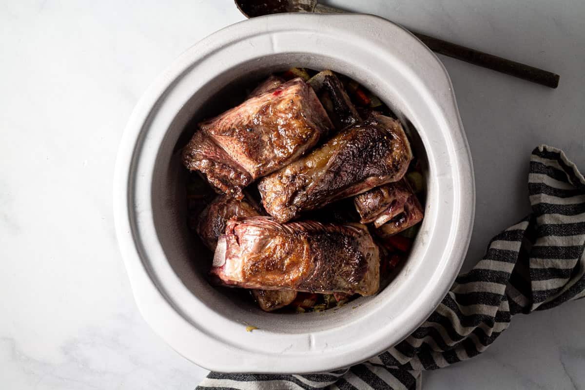 Large crock pot insert filled with seared short ribs 