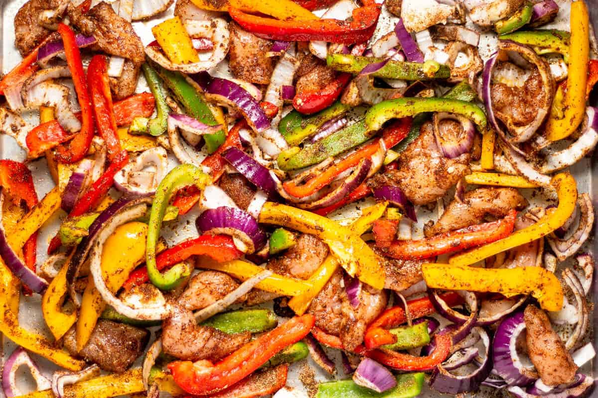 Sheet pan filled with chicken peppers and onions tossed with oil and seasonings for sheet pan fajitas