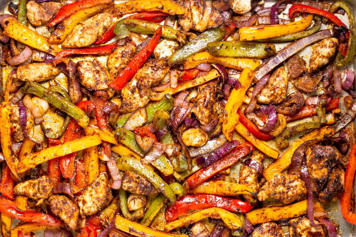 Sheet pan filled with baked chicken peppers and onions for sheet pan fajitas