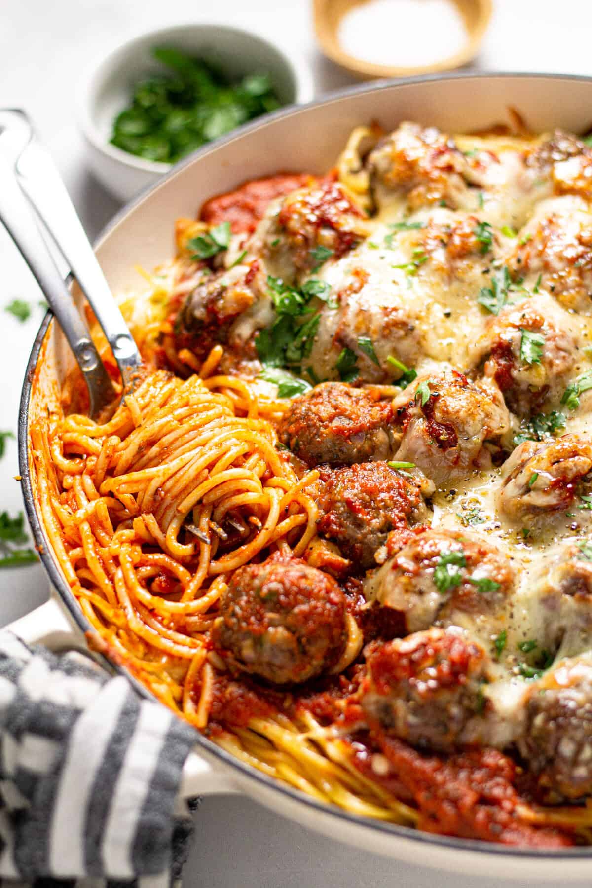 Close up shot of a pan filled with baked spaghetti and meatballs garnished with fresh parsley