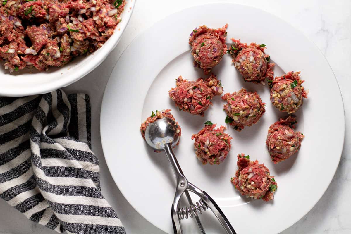 White plate with homemade meatballs being scooped onto it using a cookie scoop