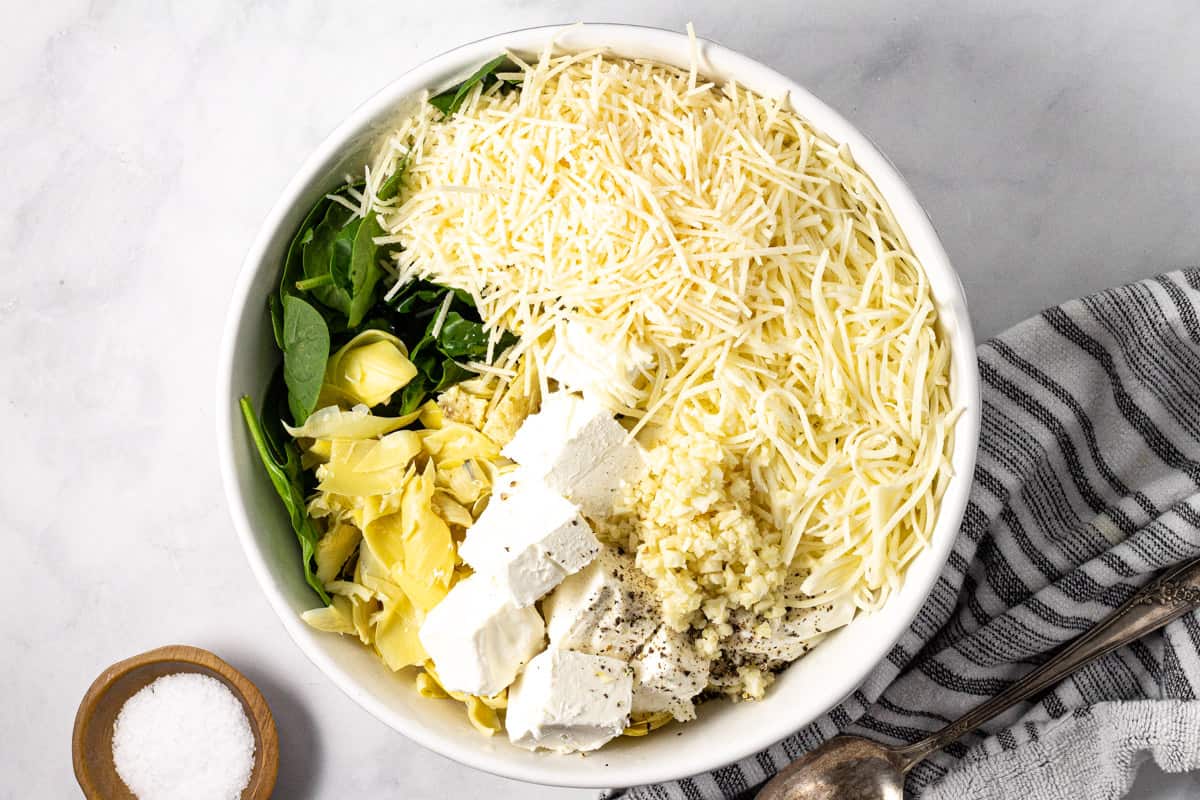 Large white bowl filled with ingredients to make spinach and artichoke dip