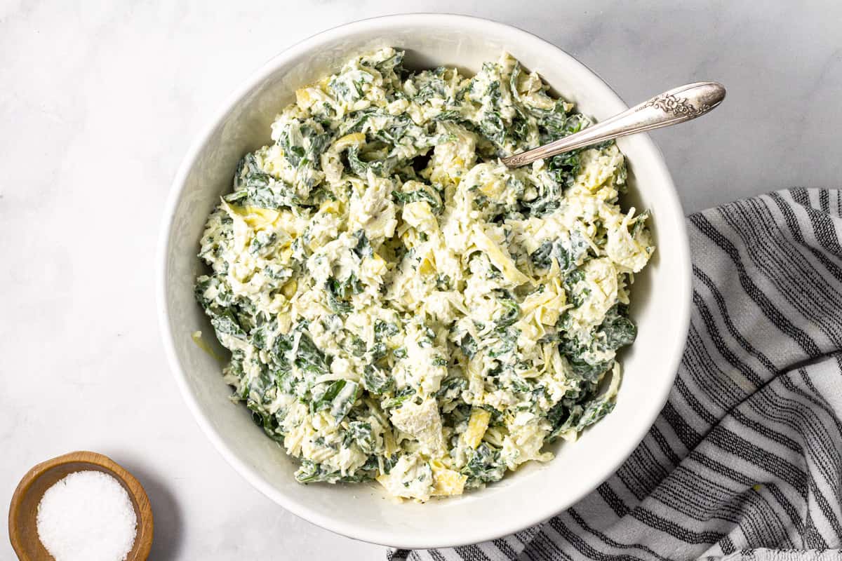 Large white bowl filled with ingredients to make spinach and artichoke dip