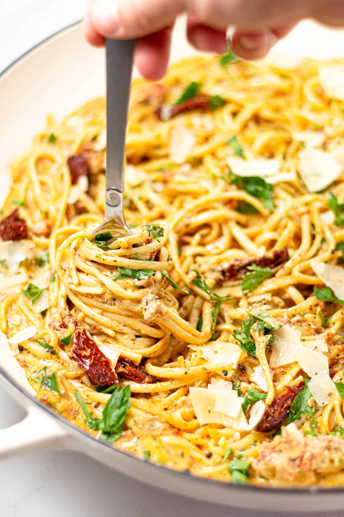 A fork twirling linguine in a large pan of sun-dried tomato pasta.