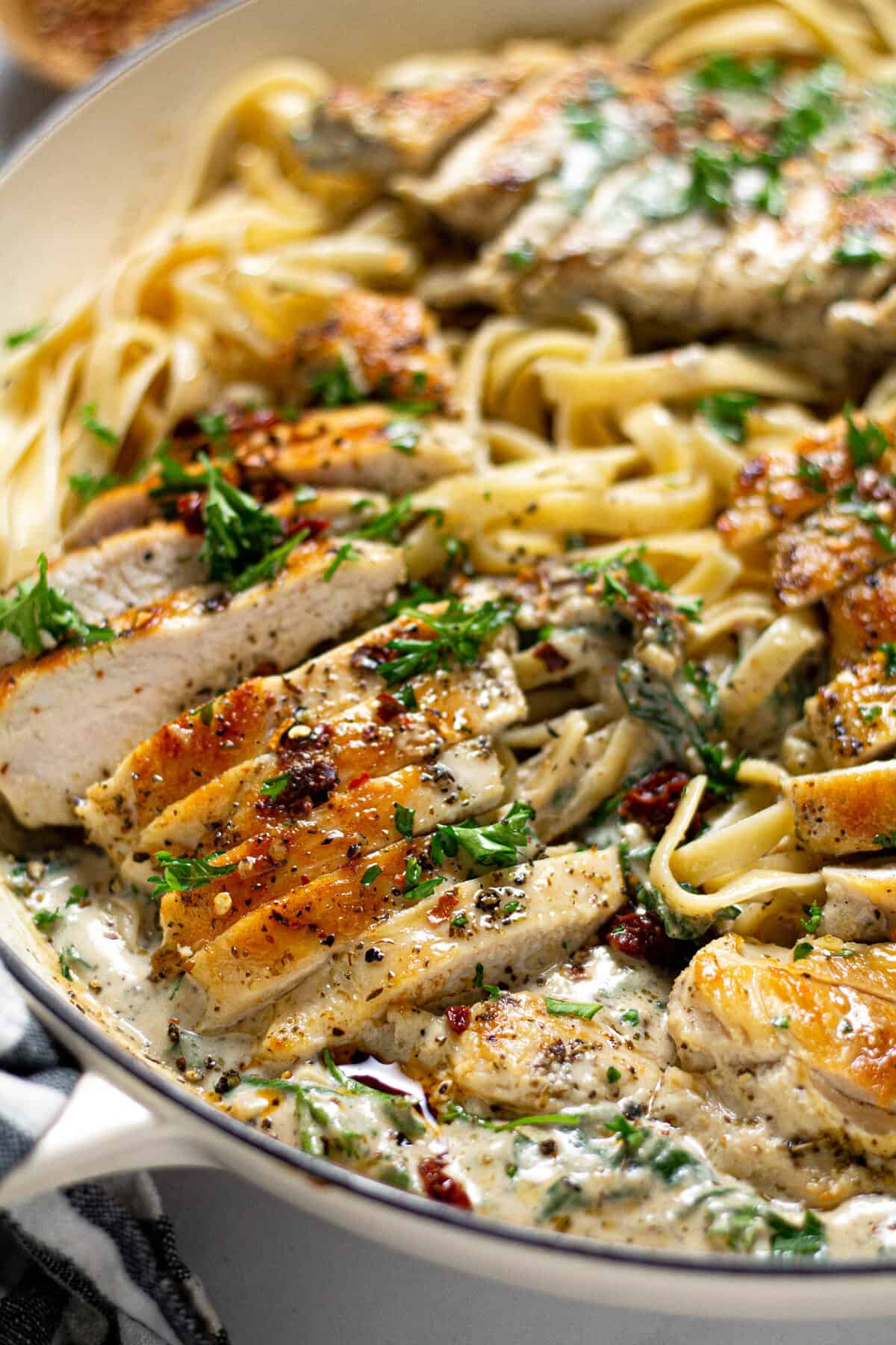 Close up shot of a pan filled with creamy Tuscan chicken over fettuccine noodles