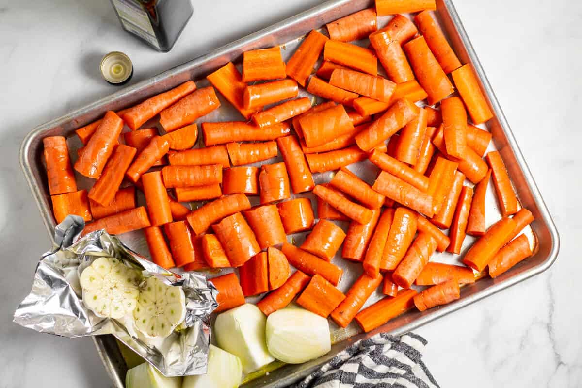 Baking sheet filled with carrots, onion and garlic drizzled with olive oil 