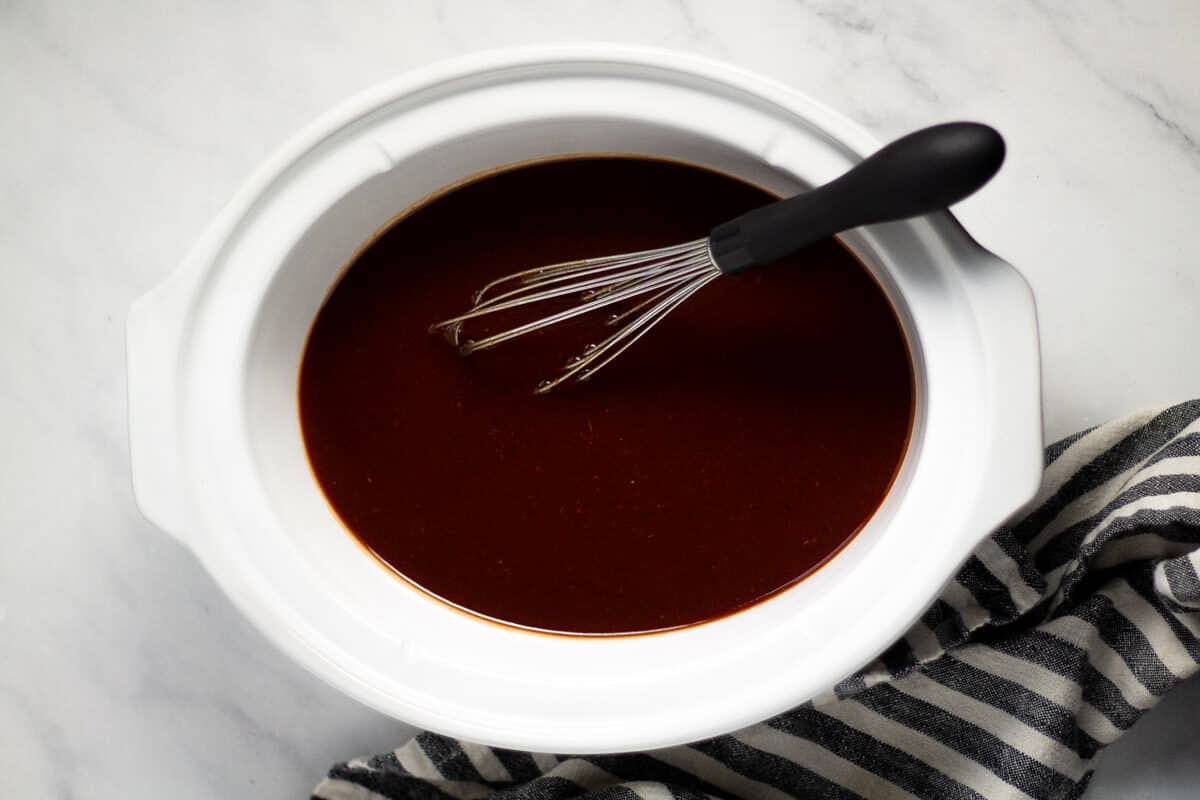 Overhead shot of an oval white crock pot insert filled with whiskey bourbon barbecue sauce