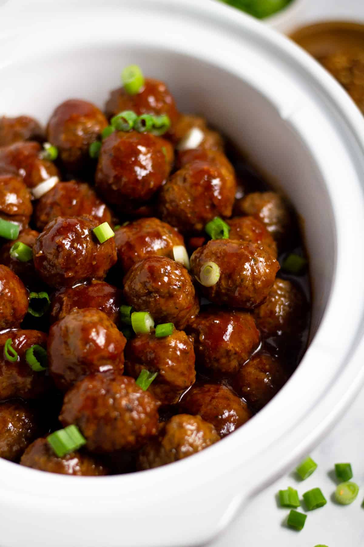 Close up shot of a white crock pot insert filled with bourbon whiskey meatballs