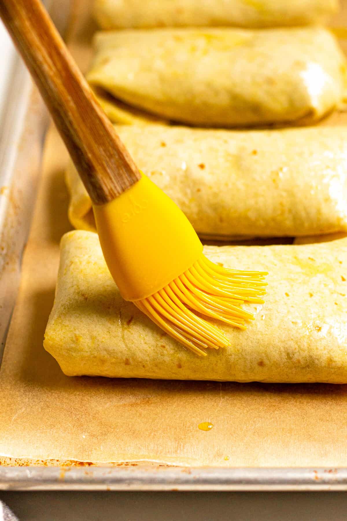 A pastry brush brushing oil over homemade beef chimichangas
