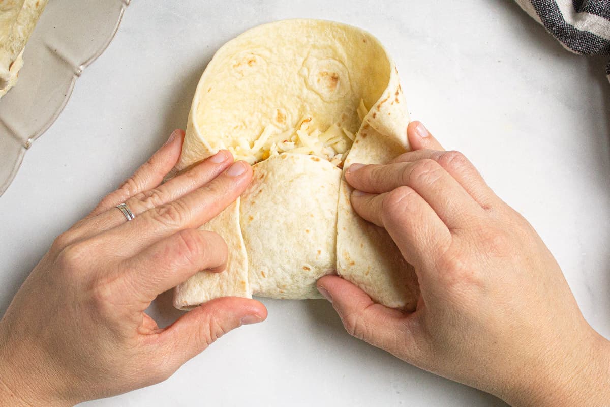 A flour tortilla being rolled into a chimichanga