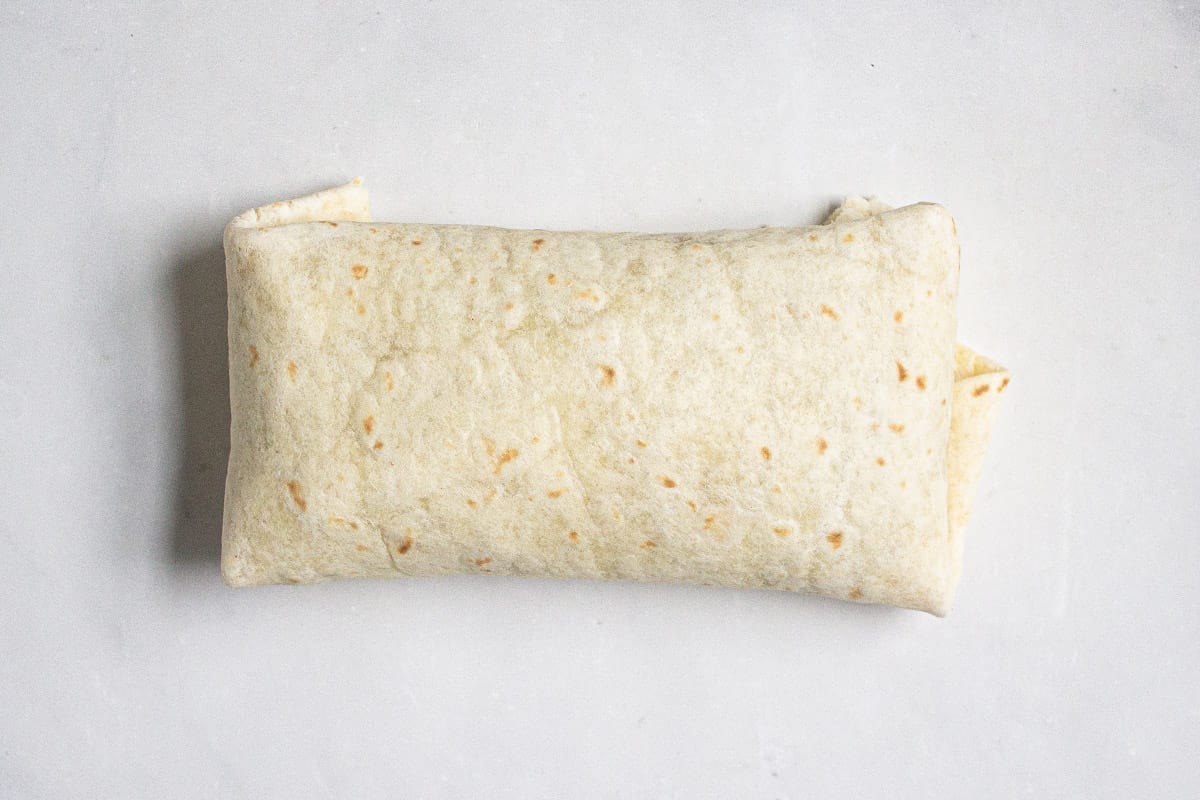 A freshly rolled chimichanga on a white marble counter top