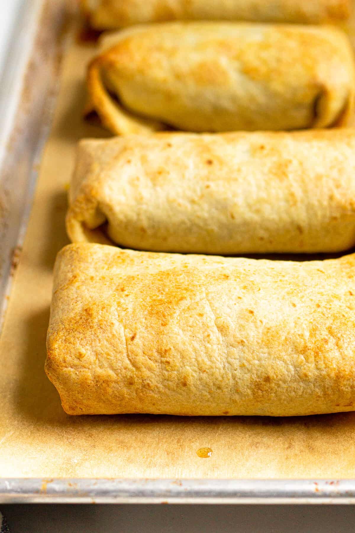 Freshly baked beef chimichangas on a parchment lined baking sheet
