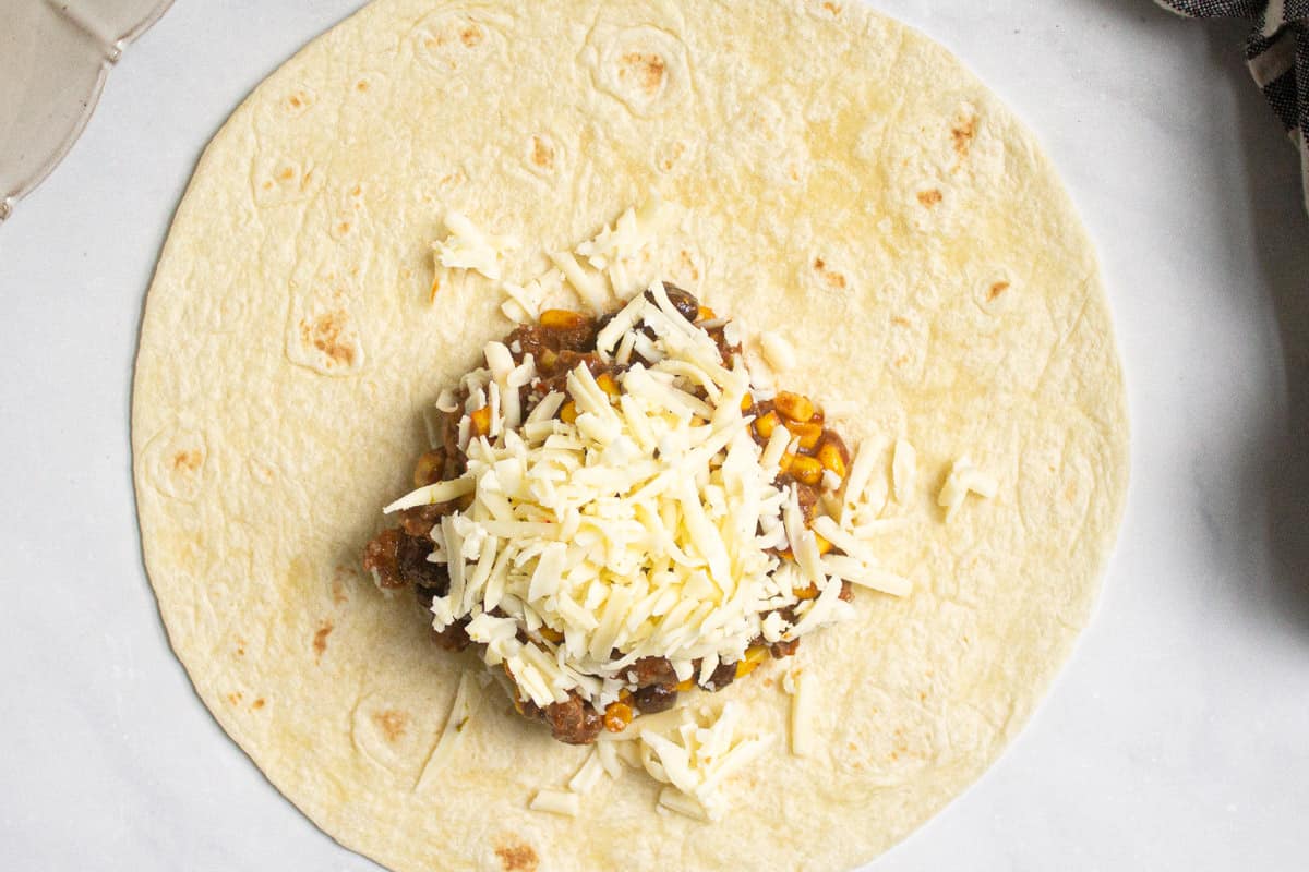 Over head shot of a flour tortilla with meat and cheese on it
