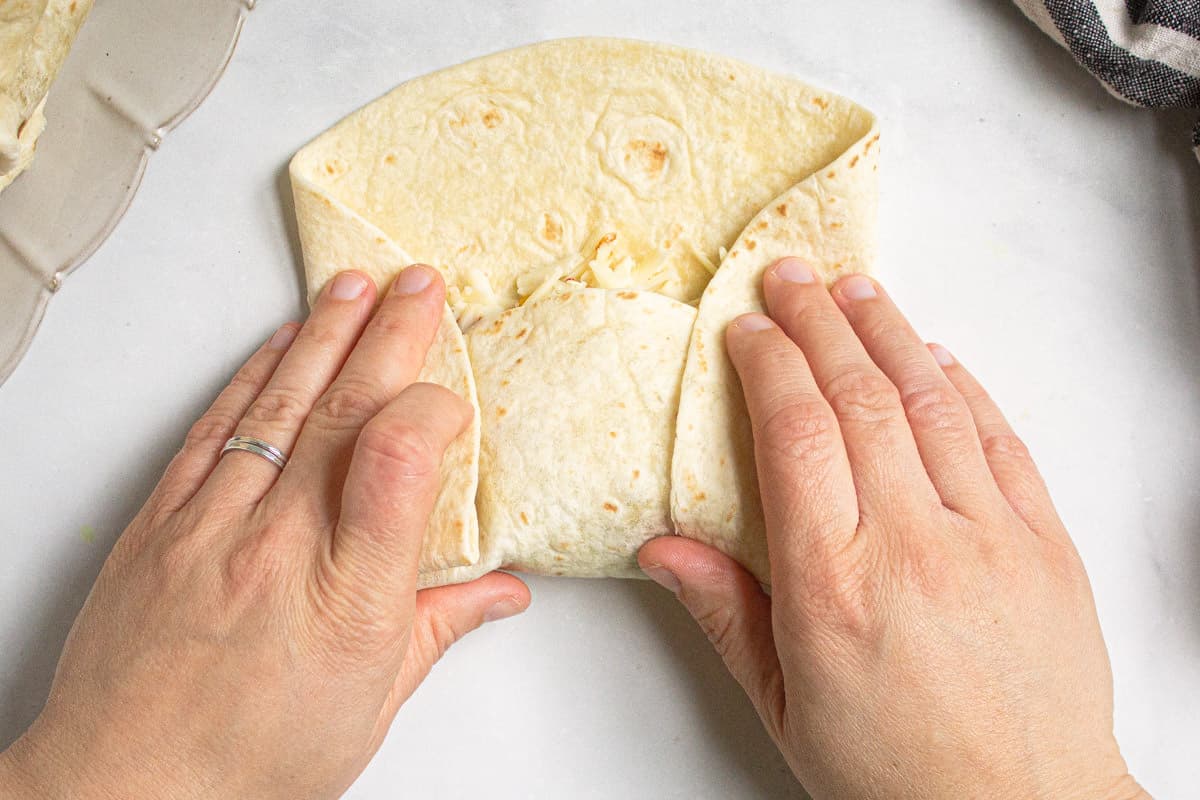 A flour tortilla being rolled into a chimichanga