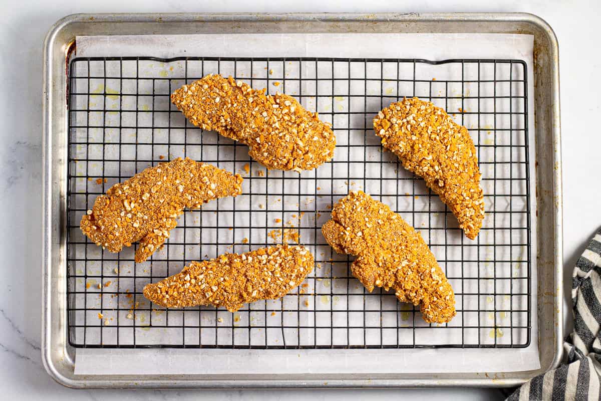 Breaded chicken tenders on a cooling rack on a parchment lined baking sheet