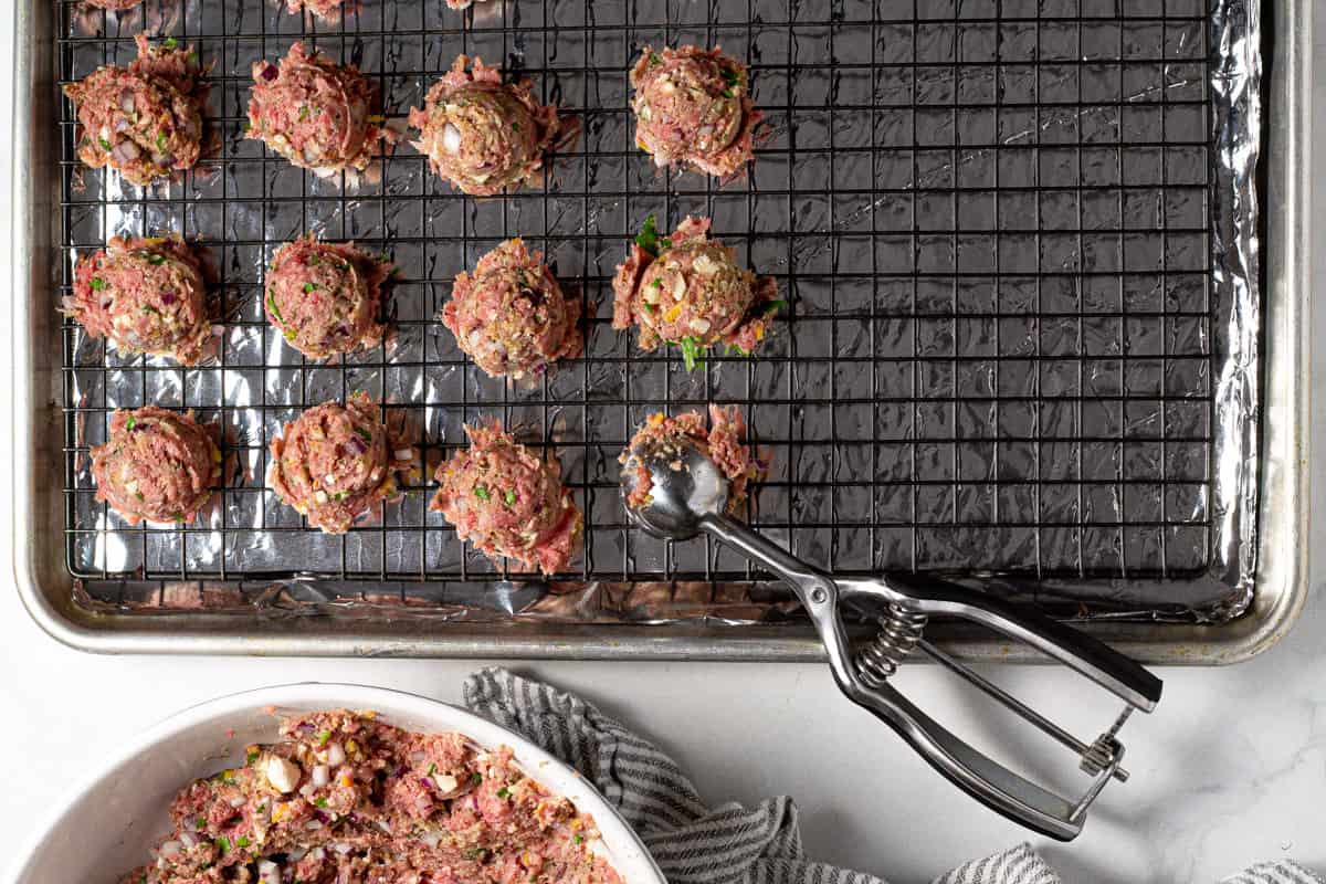 A cookie scoop scooping meatballs onto a baking sheet