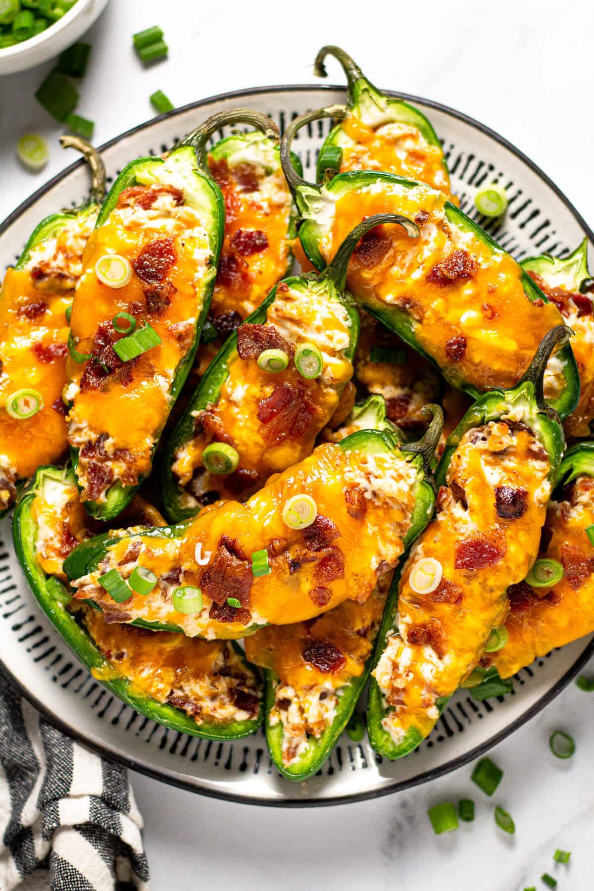 Black and white plate filled with baked jalapeno poppers garnished with green onion