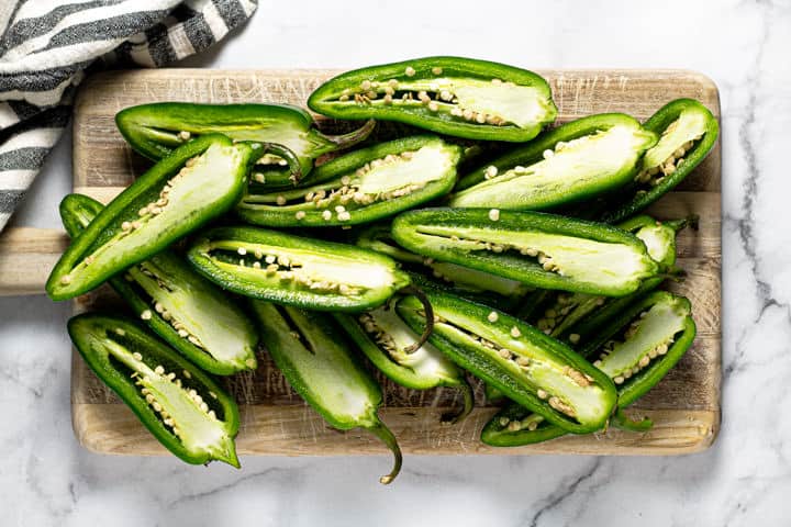 Wooden cutting board filled with jalapenos sliced in half lengthwise