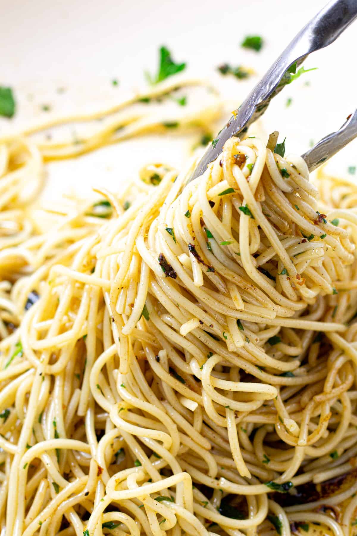 Close up shot of spaghetti being tossed in a lemon butter sauce with parsley 