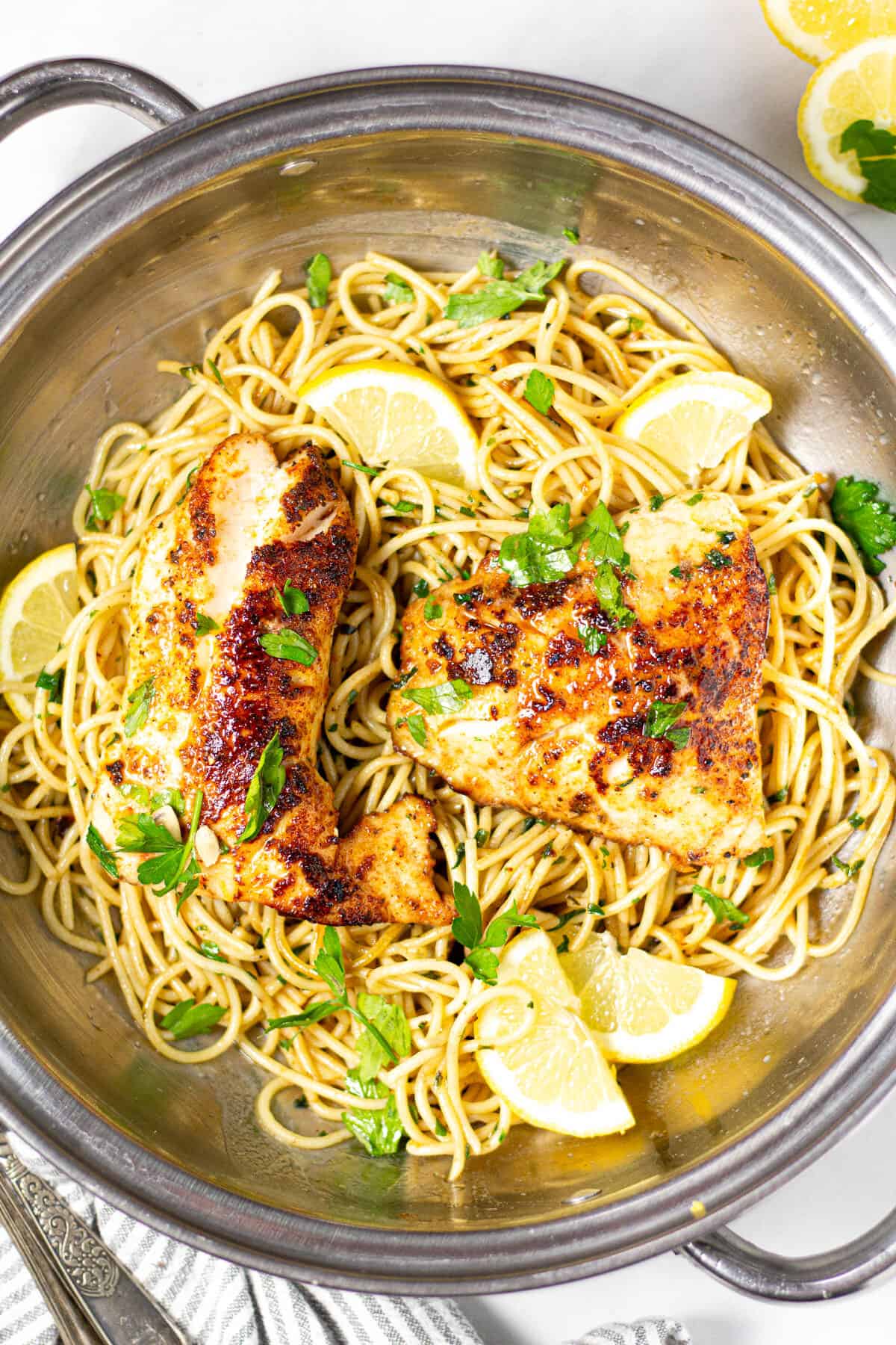 Overhead shot of lemon butter fish with spaghetti in a silver pot garnished with fresh chopped parsley 