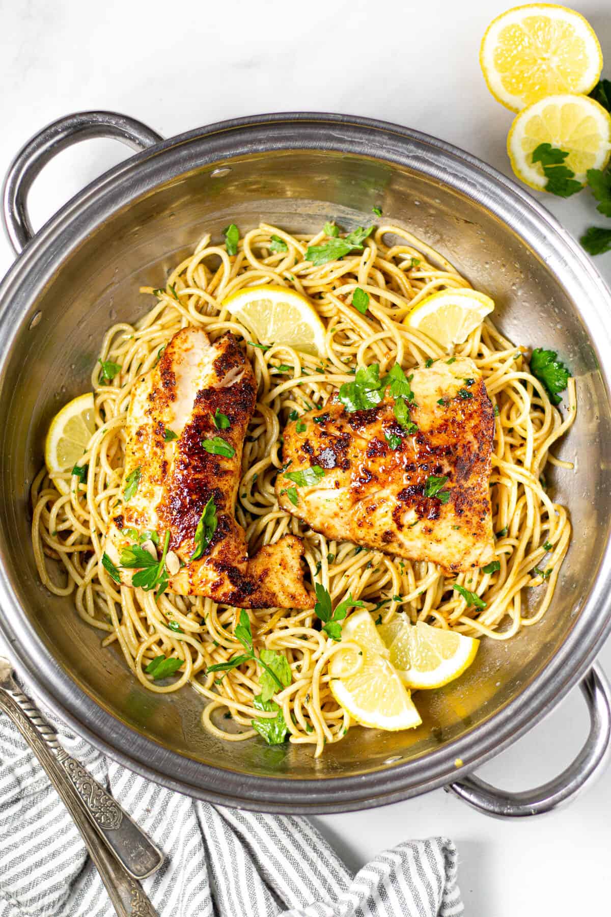 Overhead shot of lemon butter fish with spaghetti in a silver pot garnished with fresh chopped parsley 