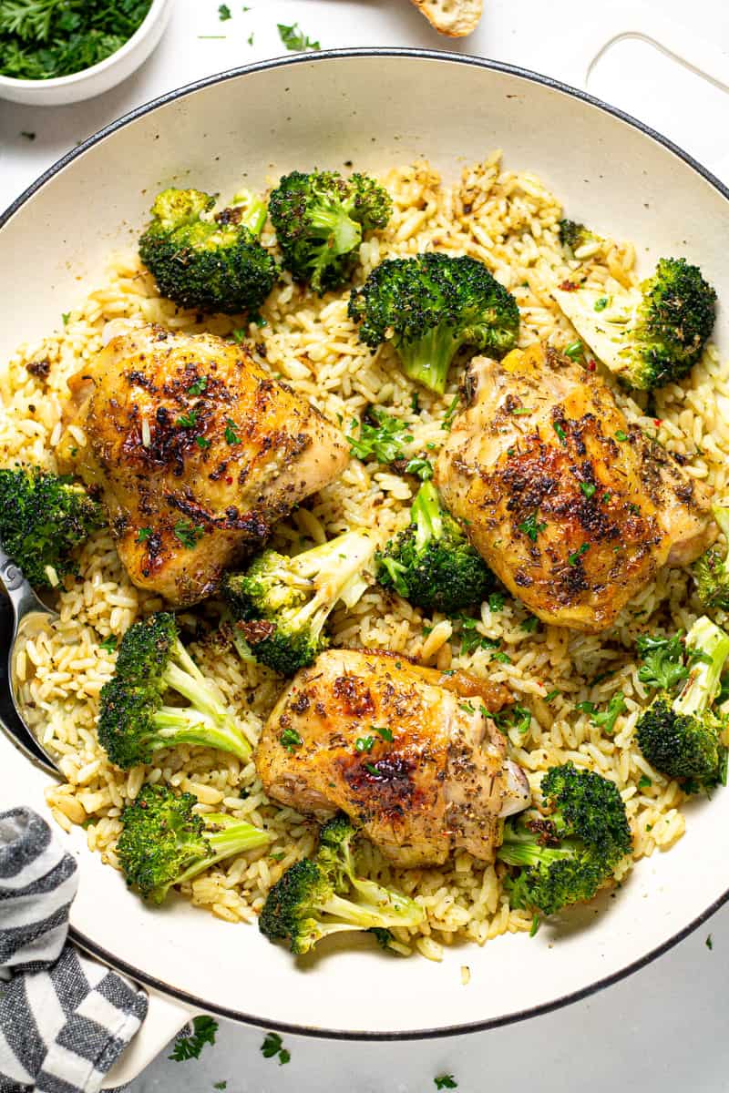 Overhead shot of a pan filled with rice pilaf broccoli and roasted chicken thighs