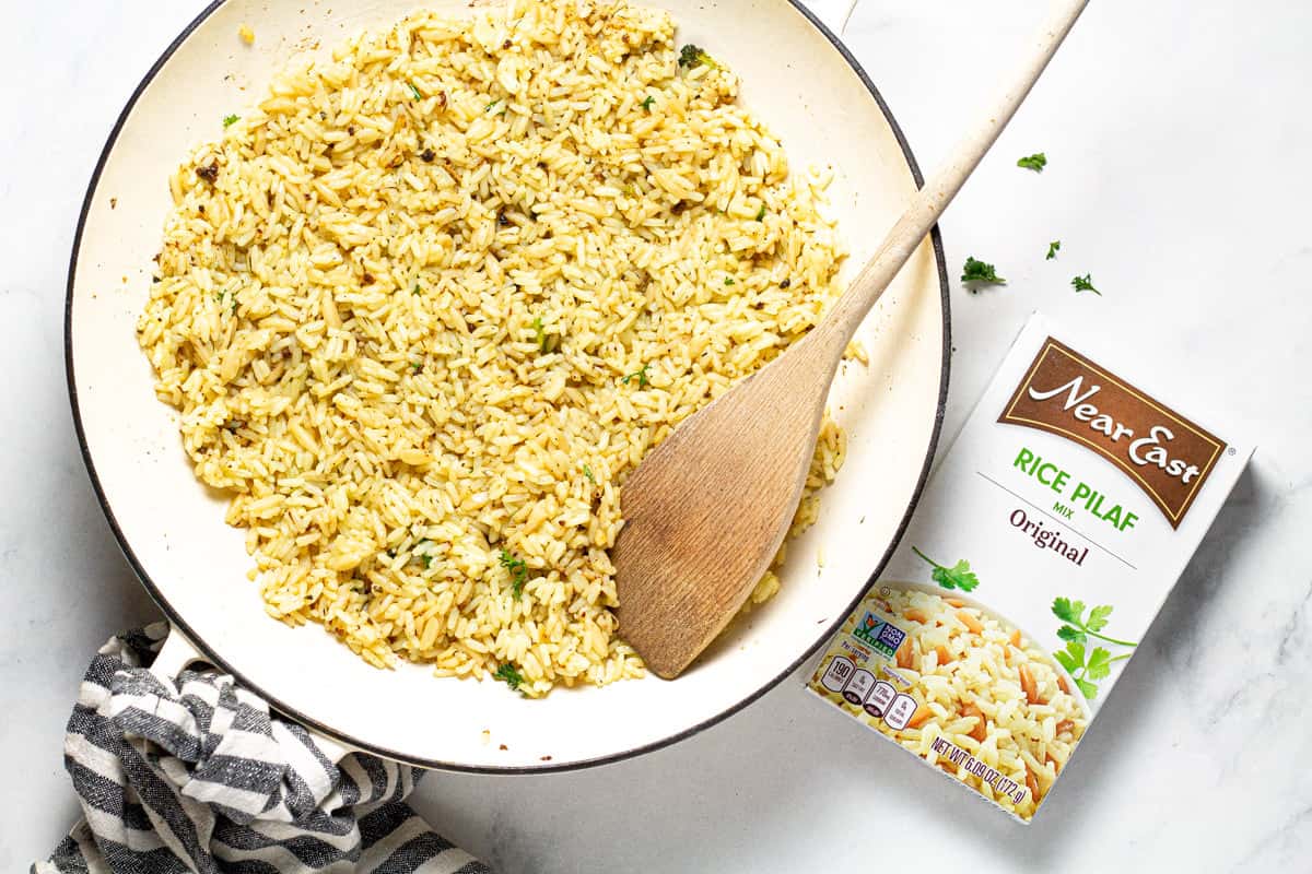 White saute pan filled with rice pilaf next to a box of Near East rice pilaf
