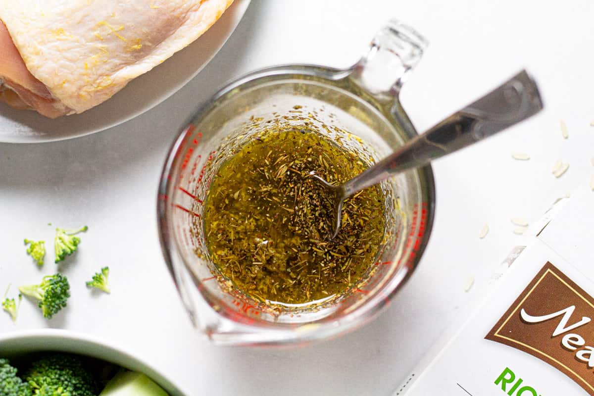 Measuring cup filled with a chicken marinade of olive oil and dried herbs