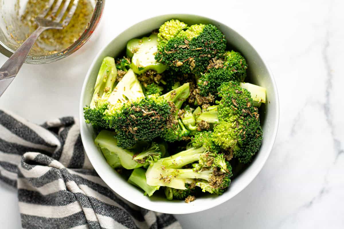 White bowl filled with broccoli tossed in olive oil and dried herbs