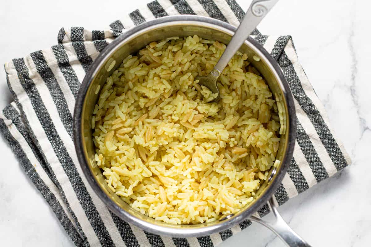Small sauce pan filled with cooked rice pilaf on a lined kitchen towel