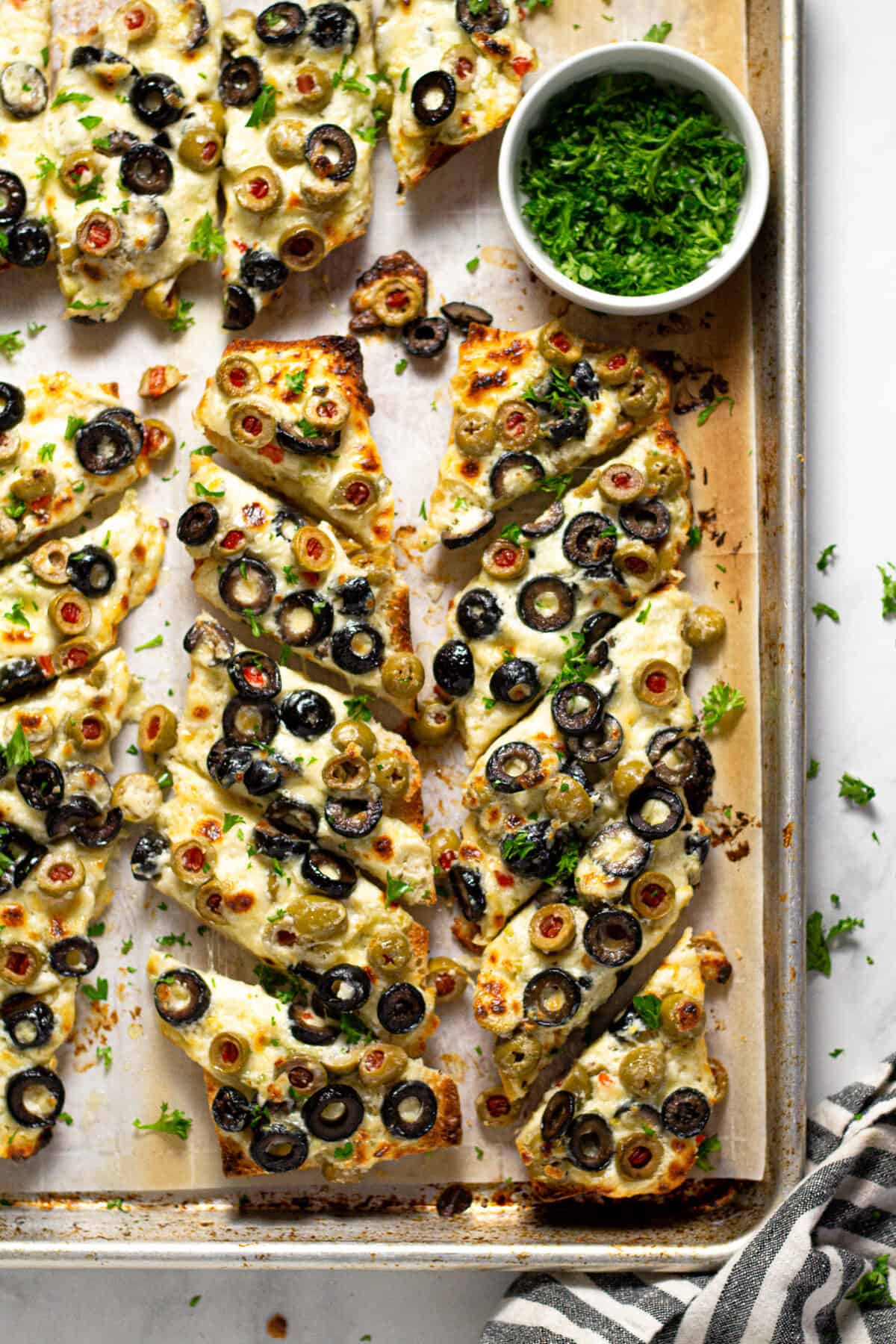 Sheet pan with olive cheese bread that is sliced and garnished with parsley 