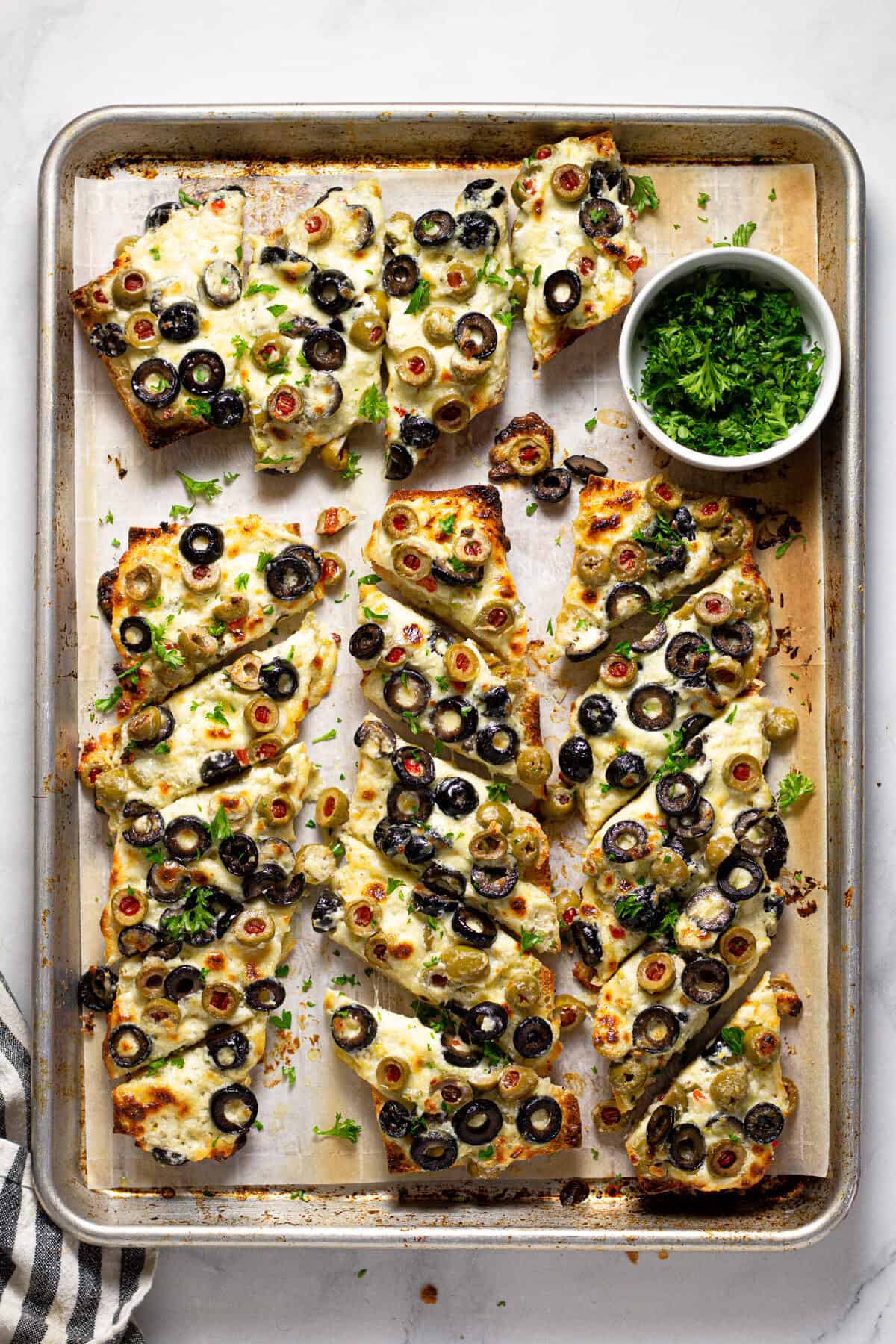 Sheet pan with olive cheese bread that is sliced and garnished with parsley 