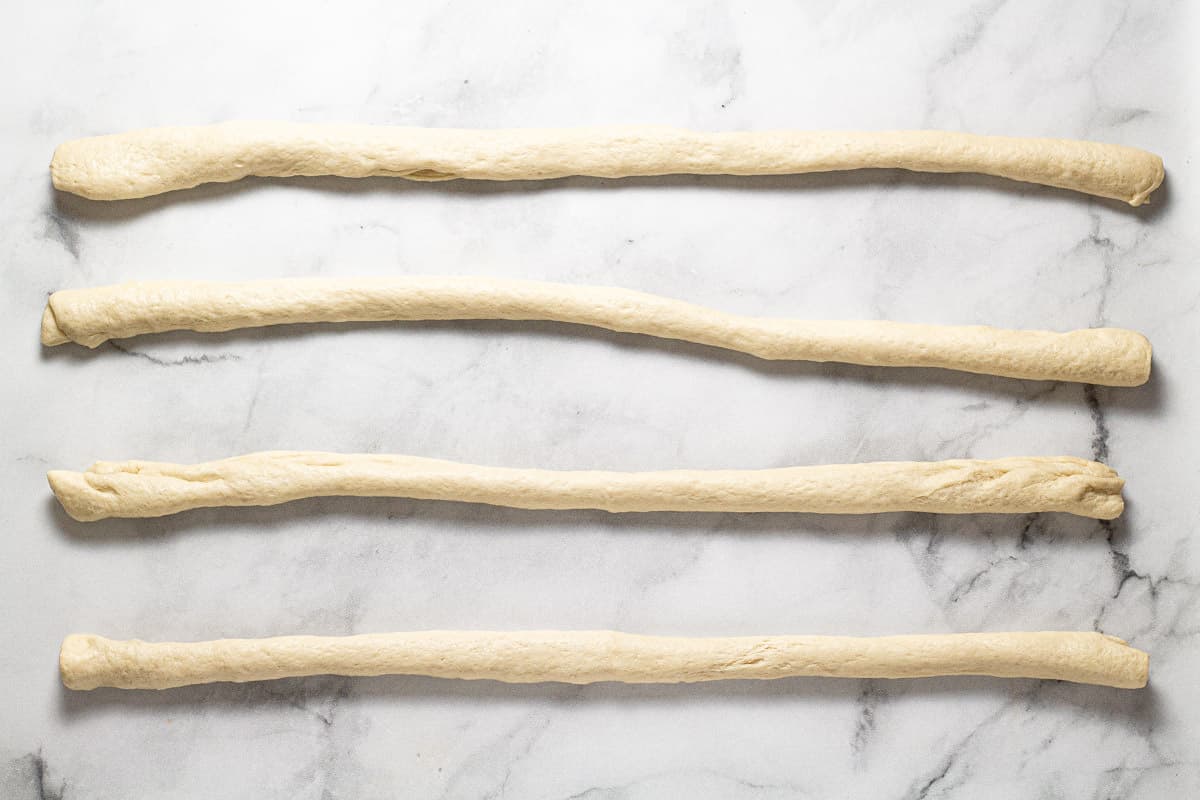A white marble counter top with pizza dough rolled into 4 ropes  