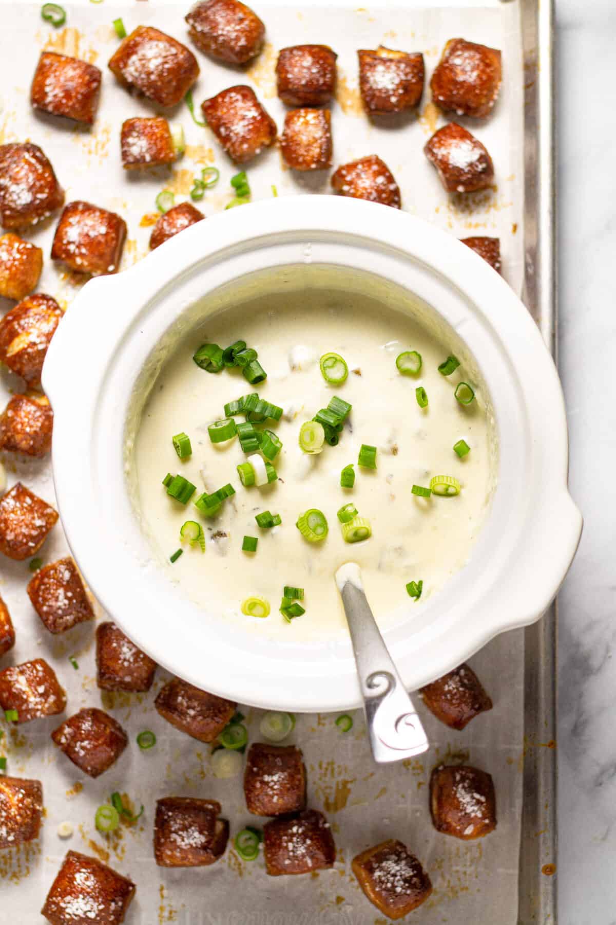 Overhead shot of a crock pot of queso on a baking sheet with pretzel bites