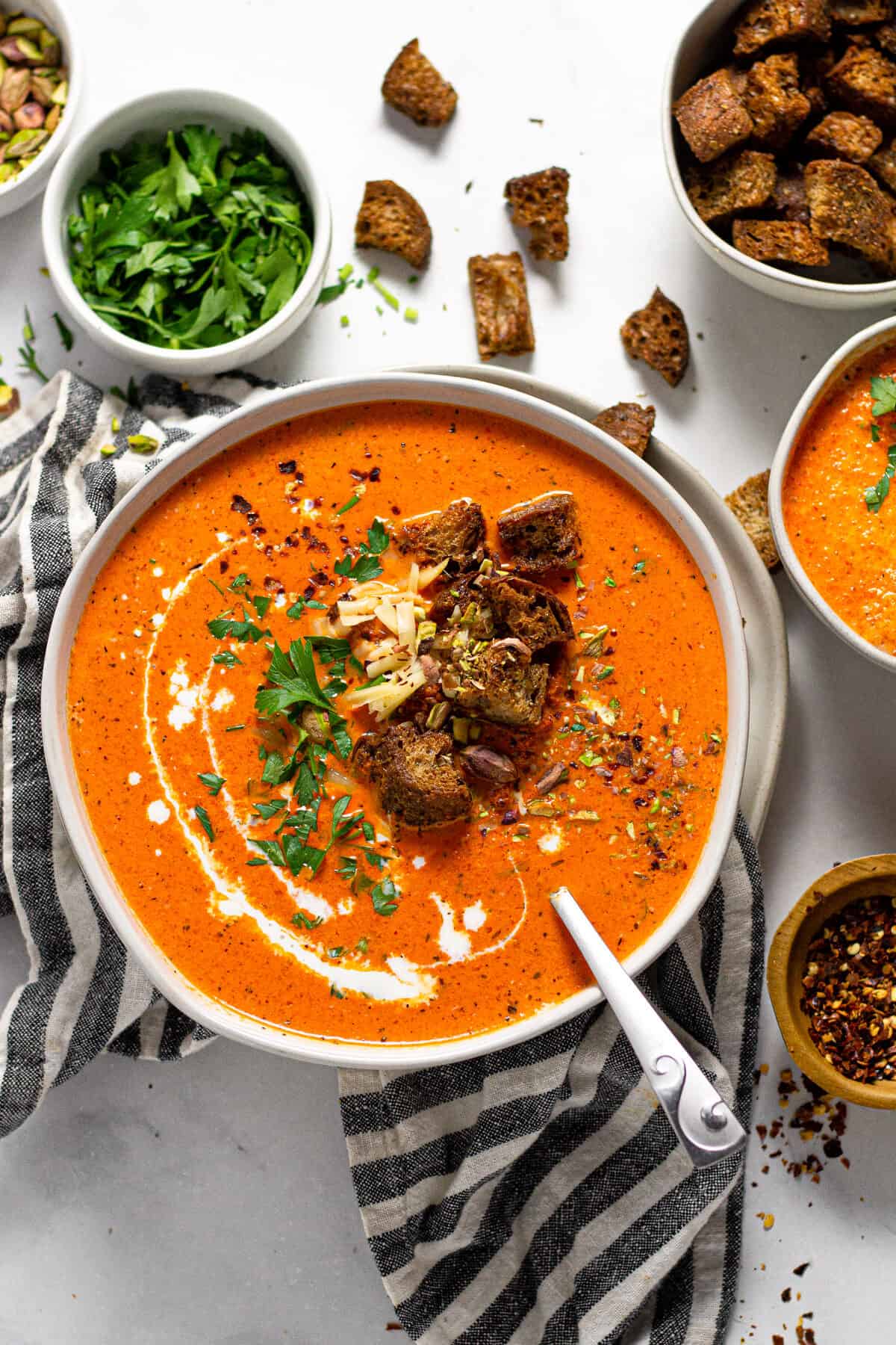Overhead shot of a bowl of roasted red pepper soup garnished with croutons and chopped parsley