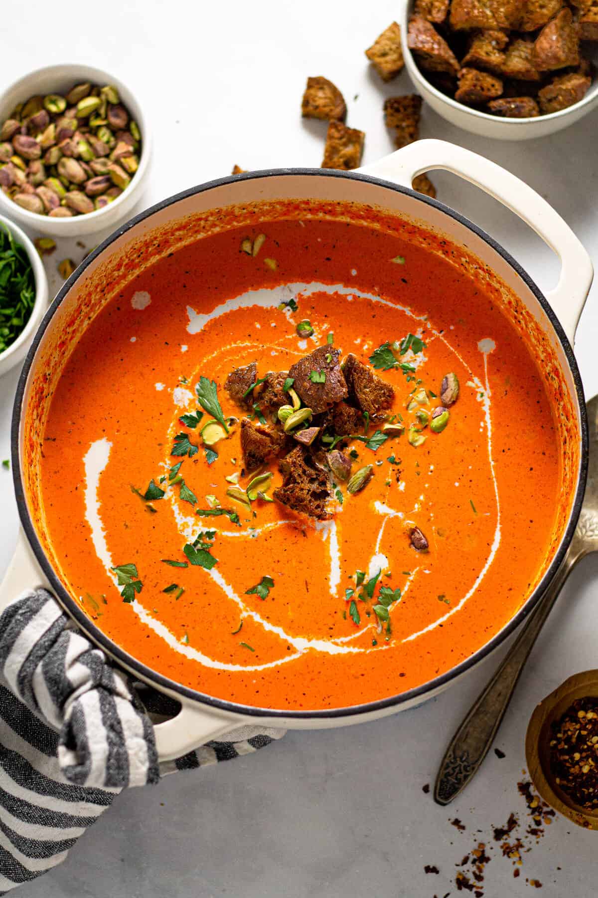 Overhead shot of a pot of roasted red pepper soup garnished with croutons and chopped parsley