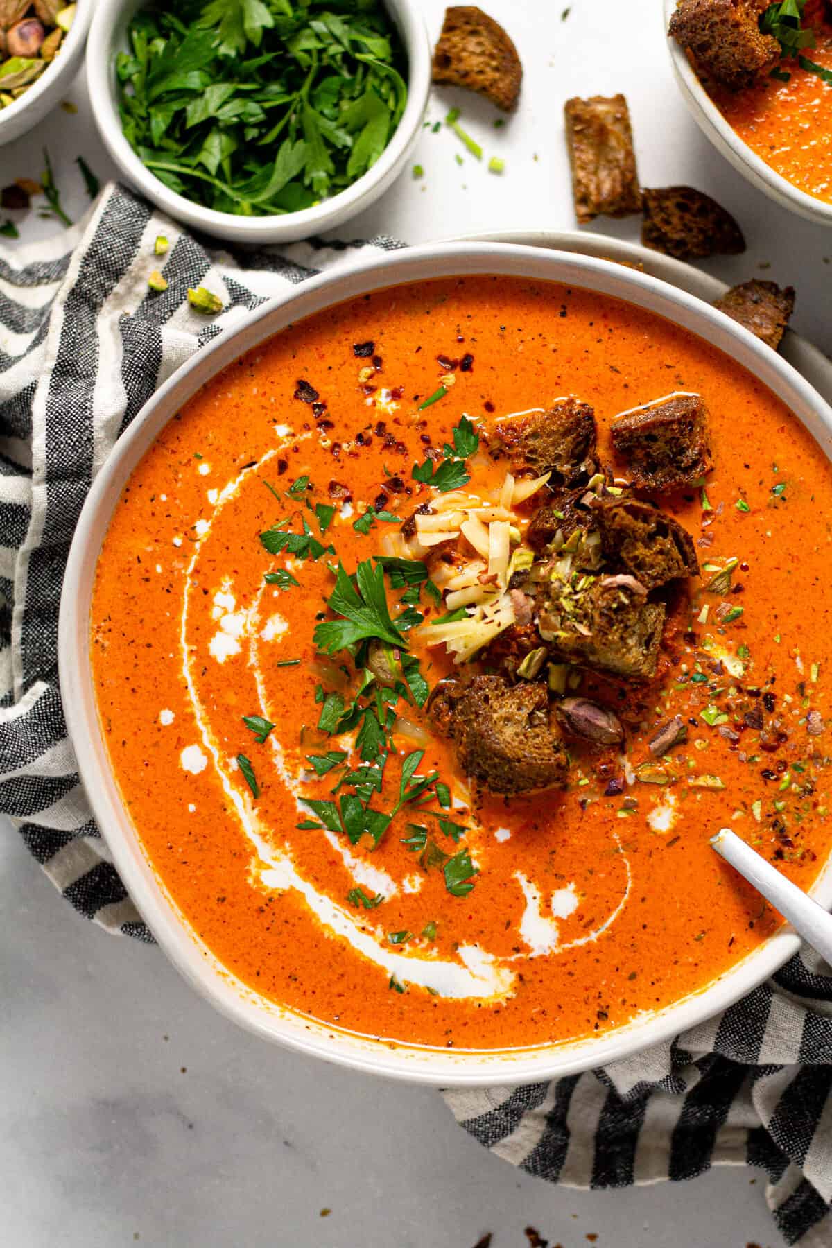 Overhead shot of a bowl of roasted red pepper soup garnished with croutons and chopped parsley