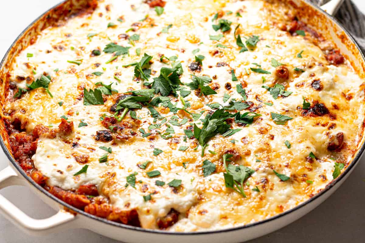Close up shot of a white pan filled with stove top lasagna garnished with fresh parsley