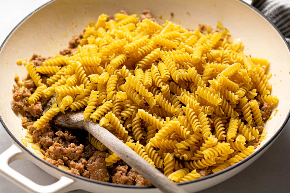 Large white pan with uncooked noodles and browned sausage