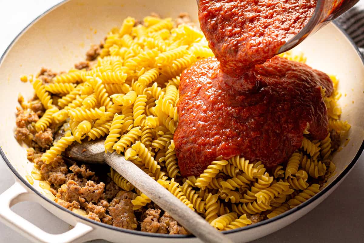 Large white pan with uncooked noodles with pasta sauce being poured in