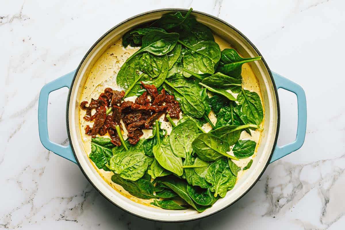Spinach and sun-dried tomatoes added to a pan of creamy sauce. 
