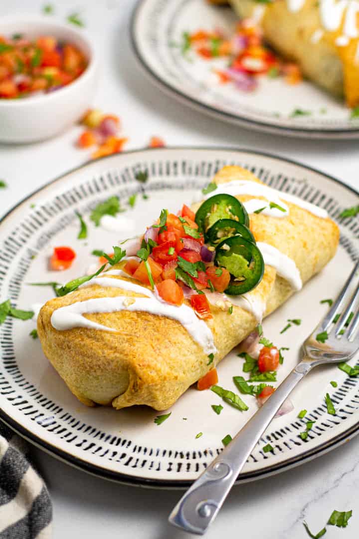 Close up shot of a baked beef enchilada on a black and white plate