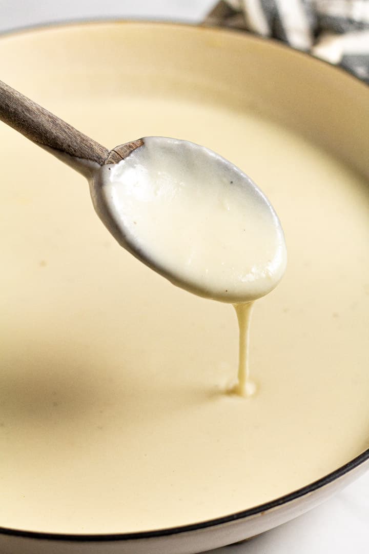 Close up of a spoon with of cheese sauce dripping off it into a pot 
