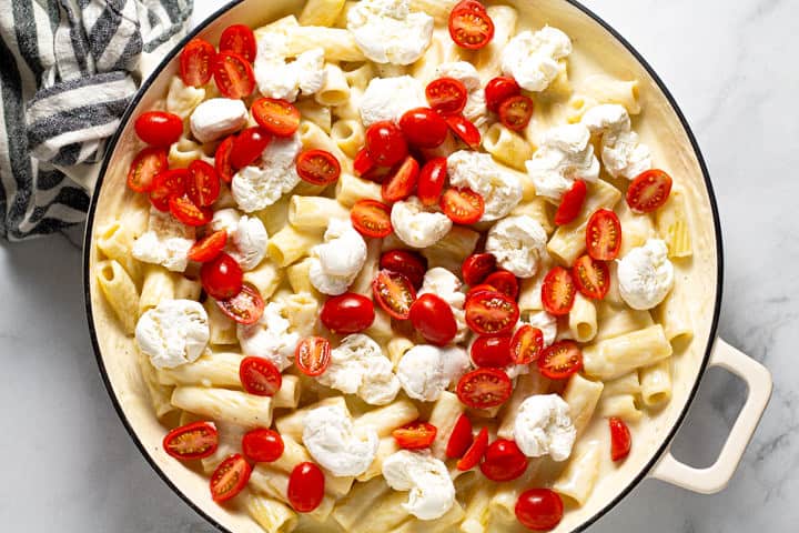 Rigatoni pasta in a creamy cheese sauce in a large white pot topped with fresh mozzarella and tomatoes