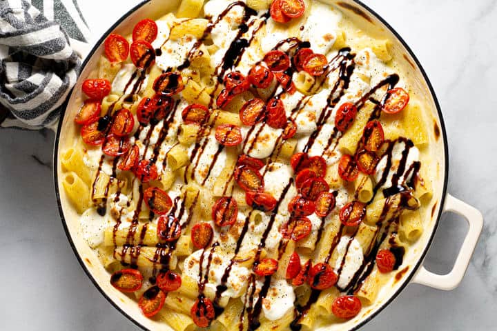 Rigatoni pasta in a creamy cheese sauce in a large white pot topped with fresh mozzarella tomatoes and balsamic glaze 
