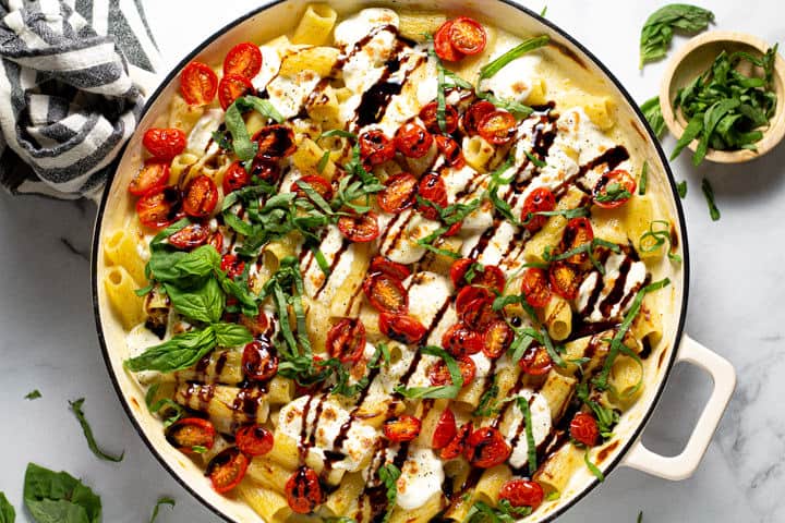 A pot of caprese mac and cheese garnished with fresh basil and balsamic glaze