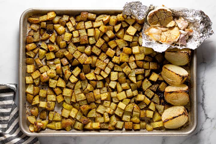 A sheet pan with roasted potatoes onions and garlic seasoned with dried herbs 