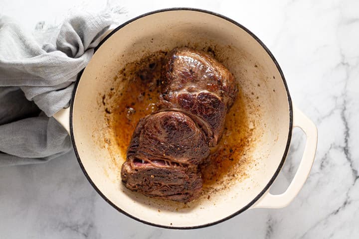 Large beef chuck roast being seared in a pot with oil