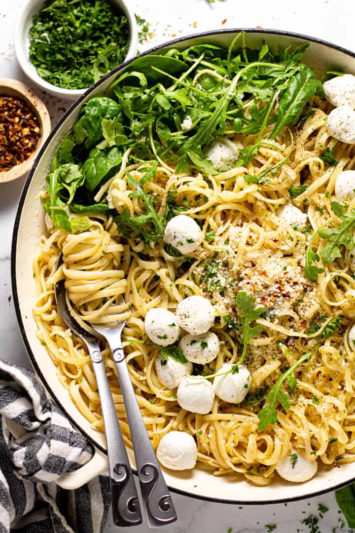 Overhead shot of a pan of garlic butter noodles garnished with Parmesan arugula and fresh mozzarella